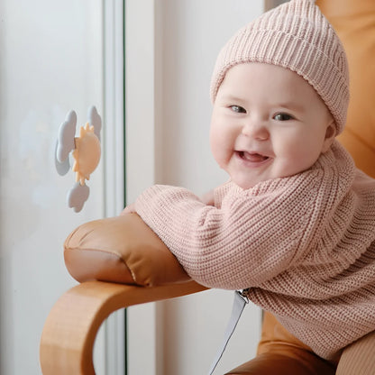 Baby trägt softes rosa geripptes strickmütze und passenden pullover spielzeug saugnapf spinner sonne