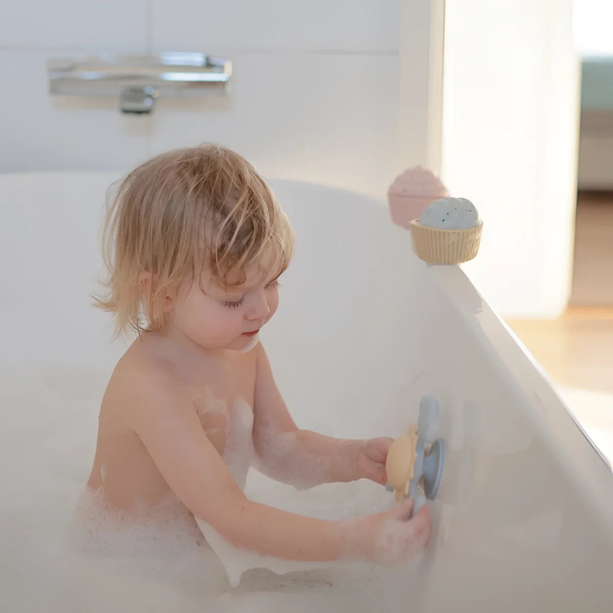 Kind mit nassem hellbraunem haar hält spielzeug saugnapf-spinner sonne aus blauem und beigem kunststoff im weißen badewanne