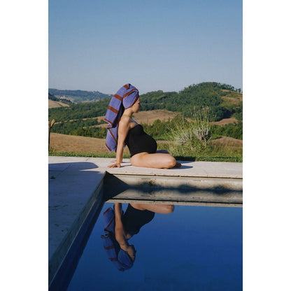 Eine schwangere frau sitzt am pool mit einem blauen und bordeaux gestreiften nachhaltigen badetuch als geschenk