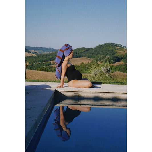 Eine schwangere frau sitzt am pool mit einem blauen und bordeaux gestreiften nachhaltigen badetuch als geschenk