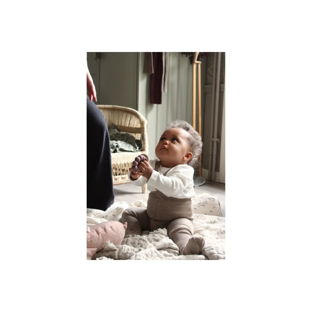 Baby sitzt auf einem flauschigen Teppich und greift nach oben in Strumpfhose mit Träger