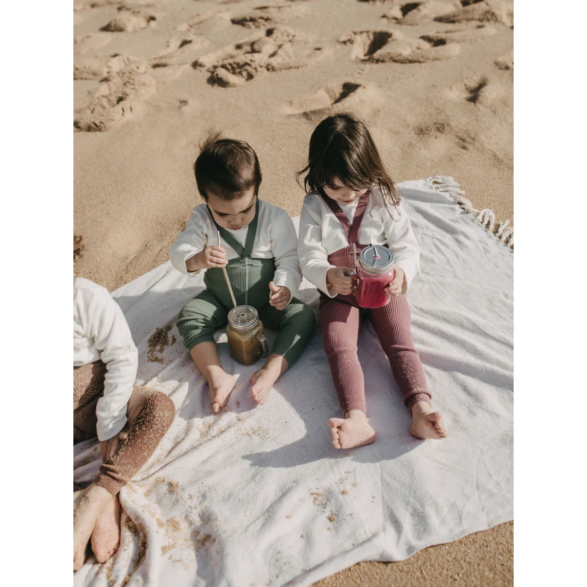 Zwei Kinder am Strand auf Decke mit Bechern, ideal für Strumpfhose mit Träger