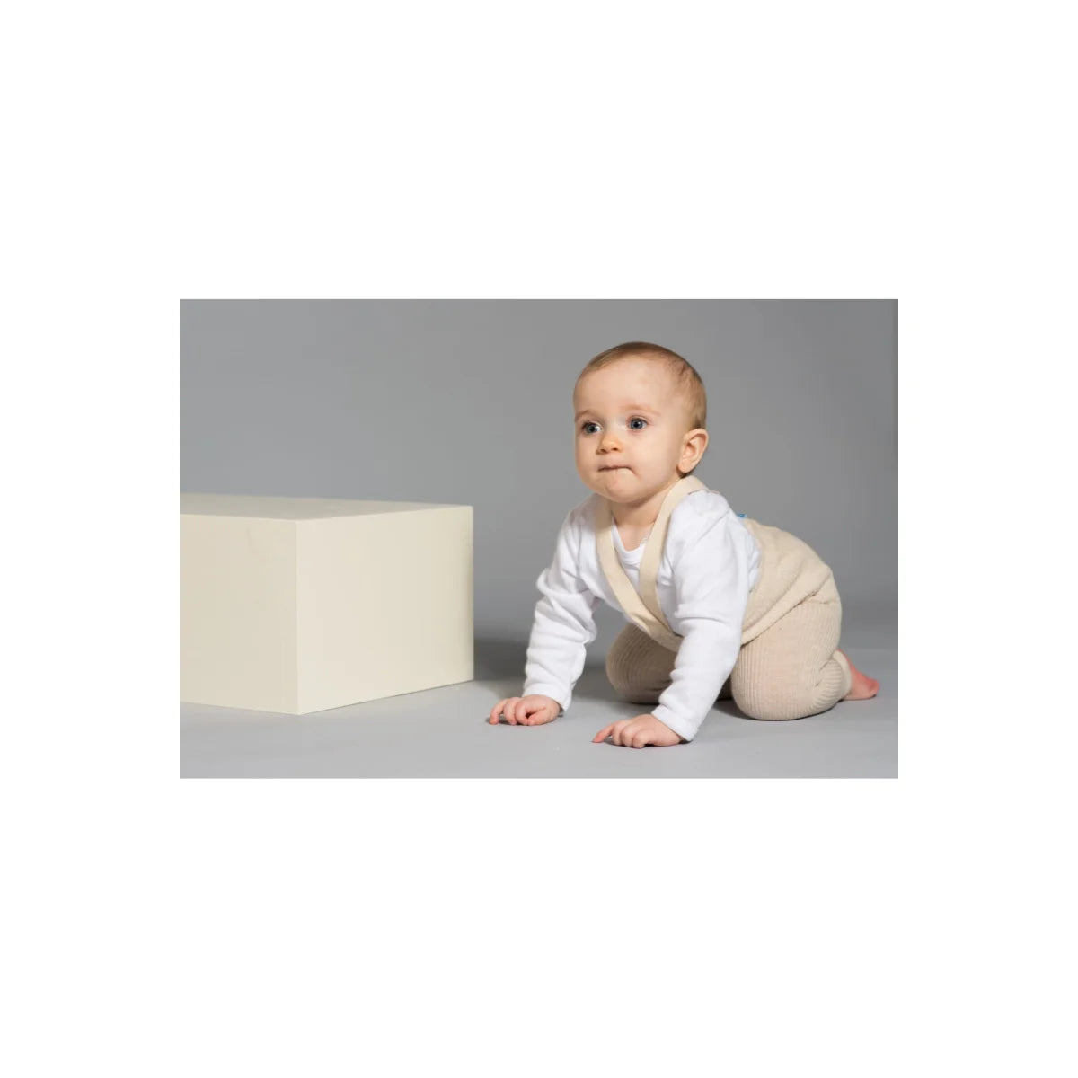 Baby krabbelt neben einem weißen Würfel, trägt Strumpfhose mit Träger in Cream Blend