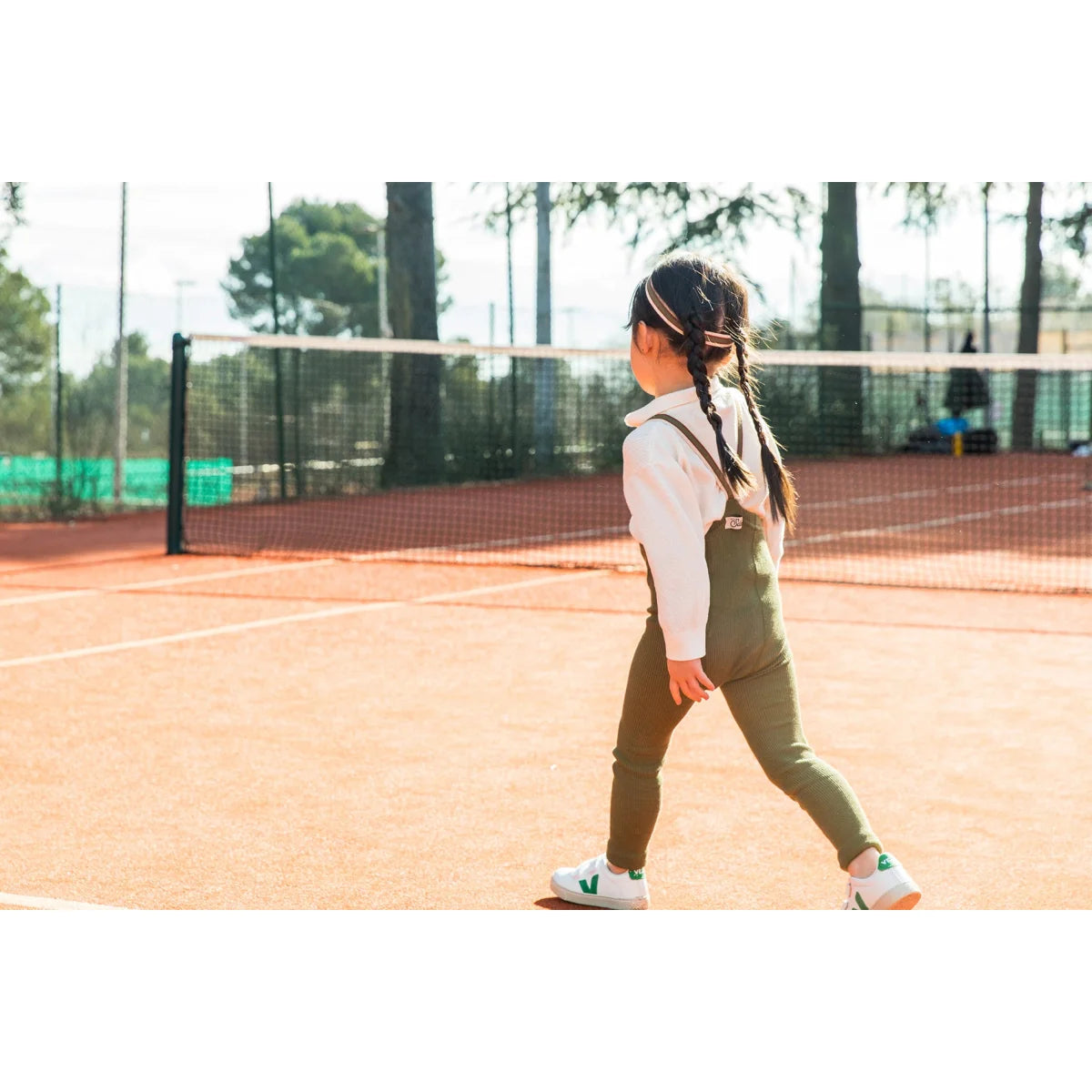 Mädchen in grünen Overalls auf einem Tennisplatz mit Strumpfhosen im Olivenstreifen