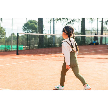 Mädchen in grünen Overalls auf einem Tennisplatz mit Strumpfhosen im Olivenstreifen