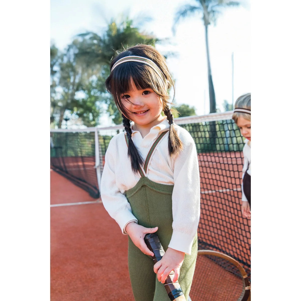 Lächelndes Mädchen mit Tennisschläger trägt olive gestreifte Strumpfhose mit Träger