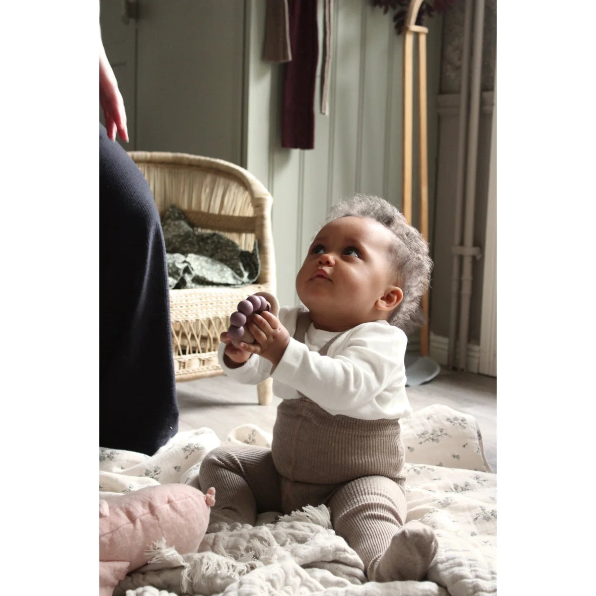 Baby auf weichem Untergrund in weißem Oberteil und gestrickten Hosen. Peanut Blend