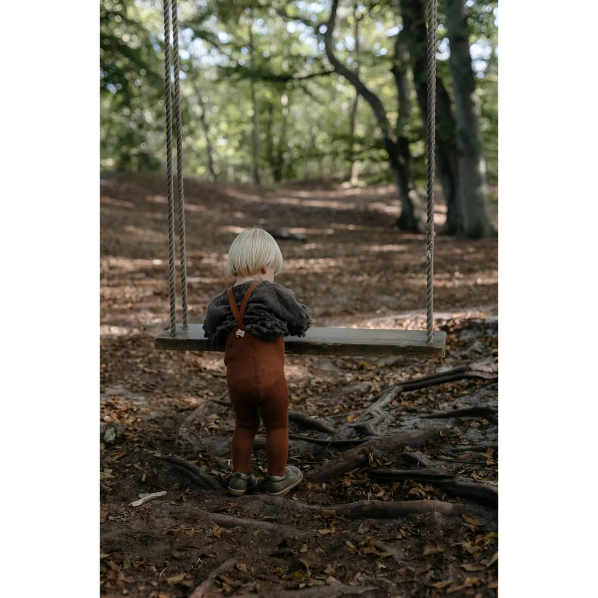 Kind auf einer Holzschaukel im Wald mit Strumpfhose mit Träger Footed in Zimt