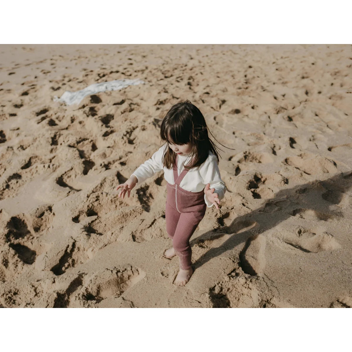 Kind spielt im Sand am Strand, getragen mit Strumpfhose mit Träger in Acai Smoothie