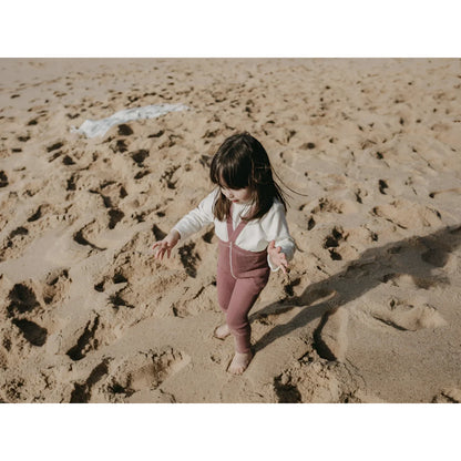 Kind spielt im Sand am Strand, getragen mit Strumpfhose mit Träger in Acai Smoothie