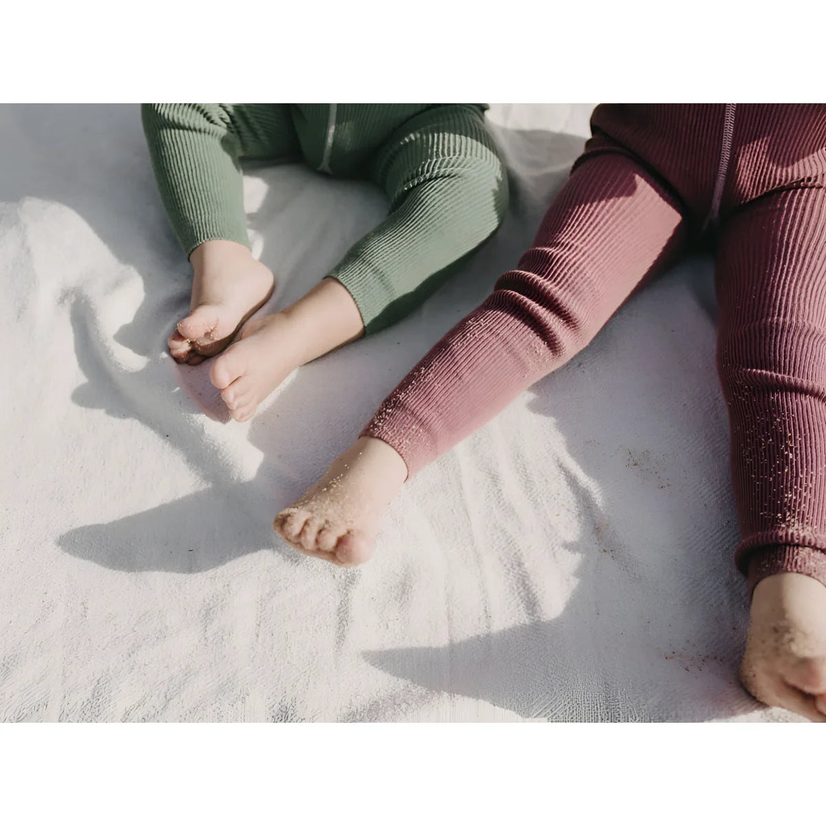 Zwei Paare Beine in grünen und rosa Ripp Leggings auf einer hellen Oberfläche