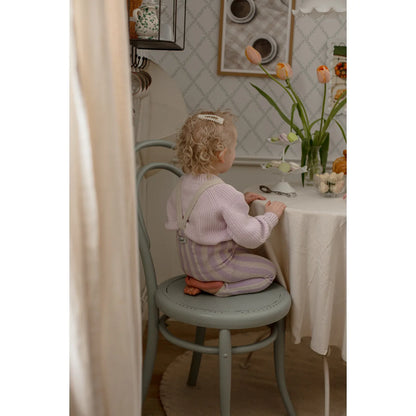 Ein kleines kind mit lockigem blondem haar trägt eine lavendel-creme strumpfhose mit trägern und sitzt auf einem grauen stuhl