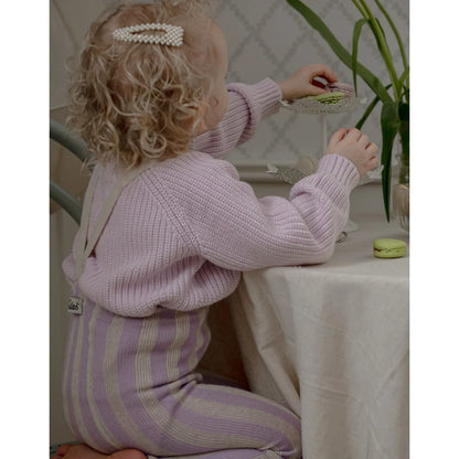 Ein kind trägt eine strumpfhose mit träger footless in lavendel und creme aus gestricktem material mit perlenhaarclip
