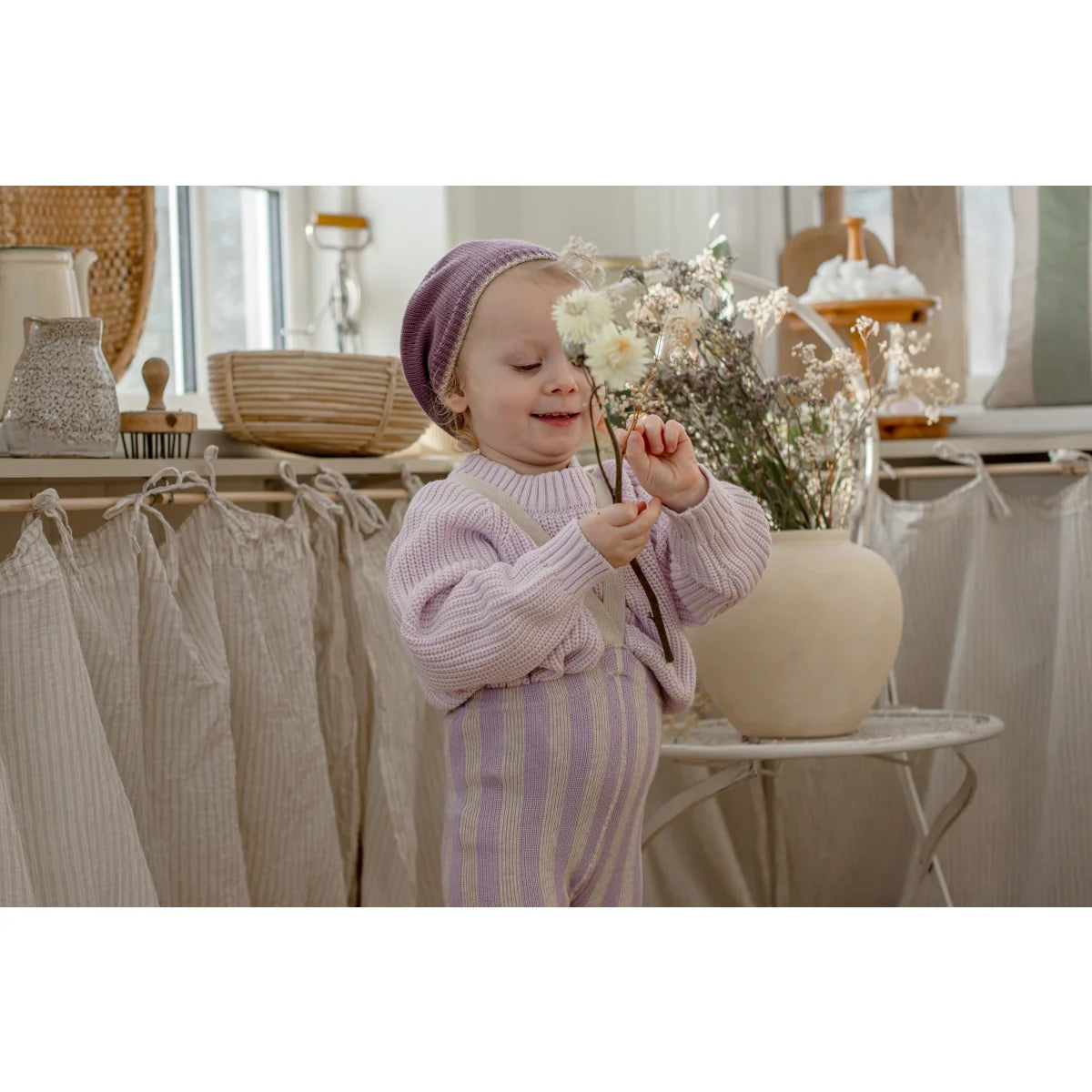 Ein kleinkind trägt eine strumpfhose mit träger footless in lavendel und creme und hält weiße blumen