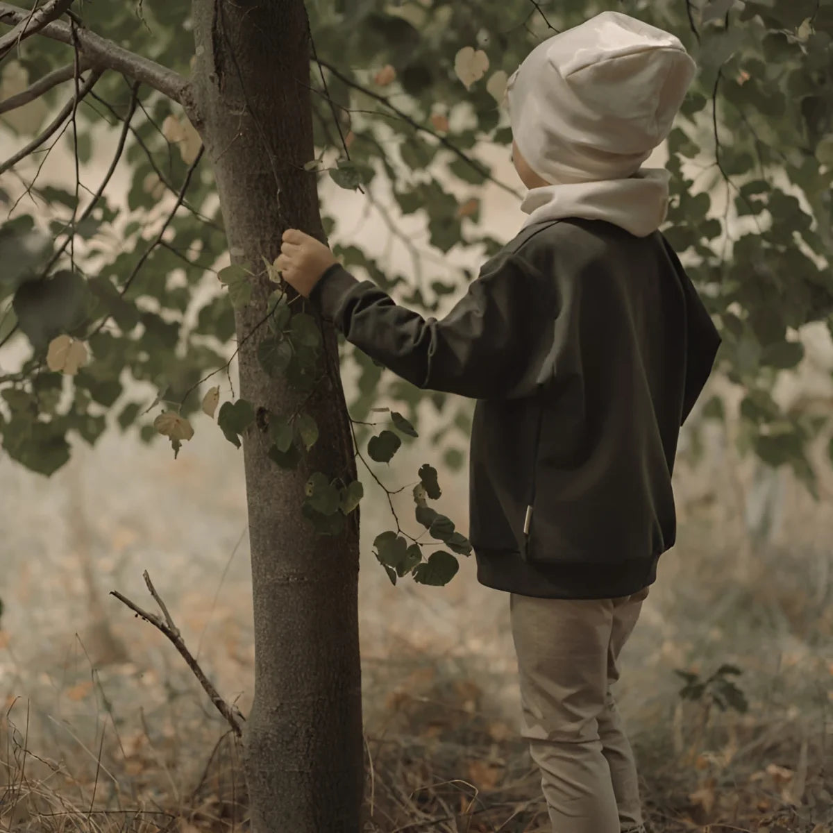 Kinderoutfit mit dunkelgrauem Sweater, hellbraunen Hosen, cremefarbenem Beanie und Schal