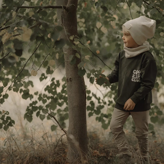 Junges Kind in dunklem Langarmshirt, hellen Hosen, passender Beanie und Nackenwärmer