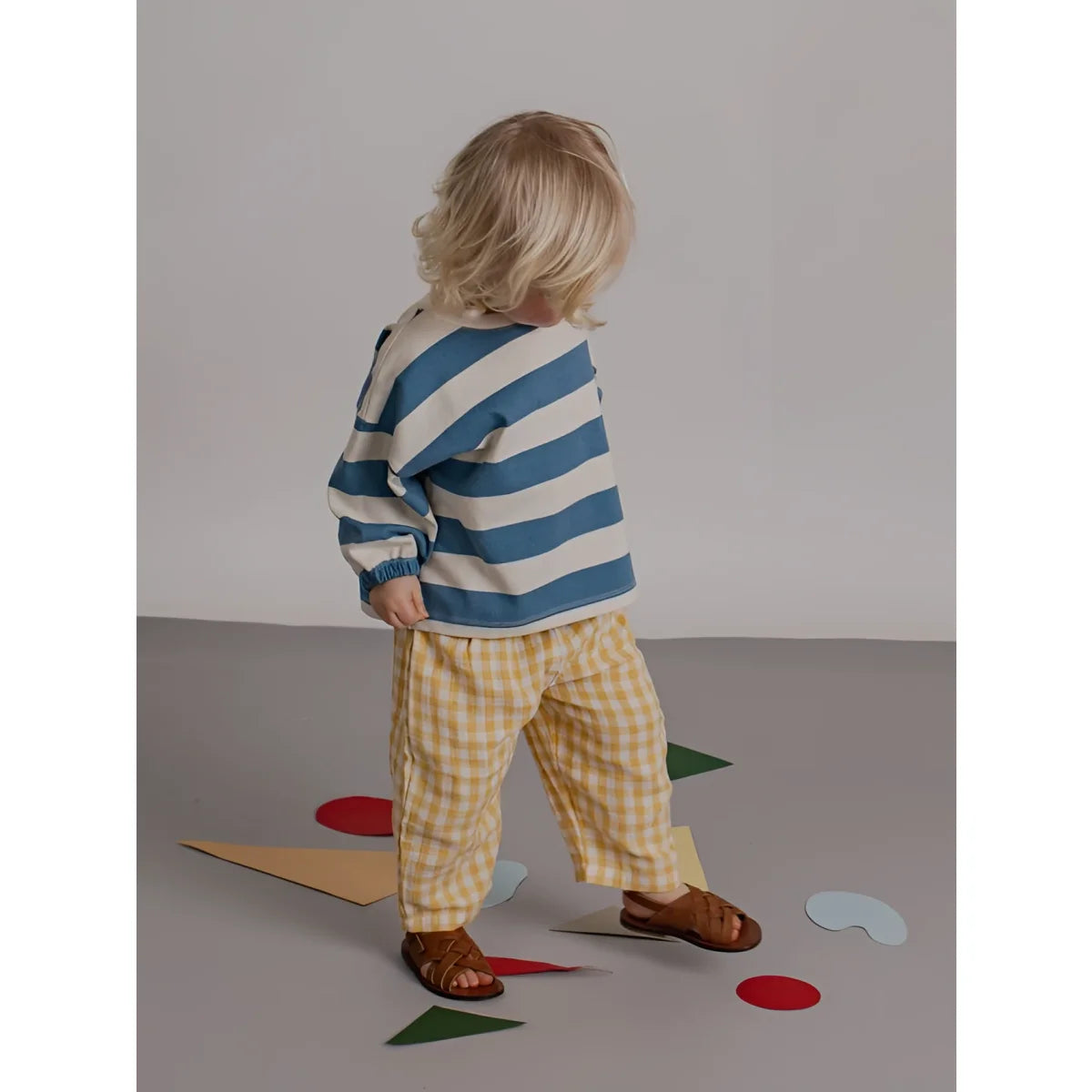 Kind trägt ein sweatshirt deck chair stripes mit blau weißen streifen langarm und gelb karierten hosen