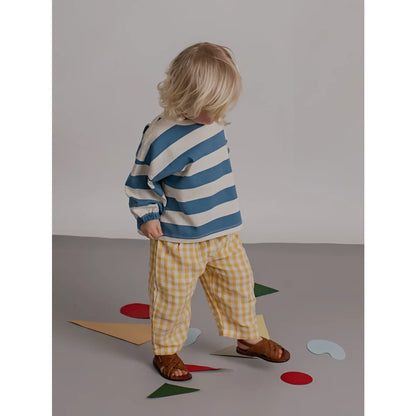 Kind trägt ein sweatshirt deck chair stripes mit blau weißen streifen langarm und gelb karierten hosen