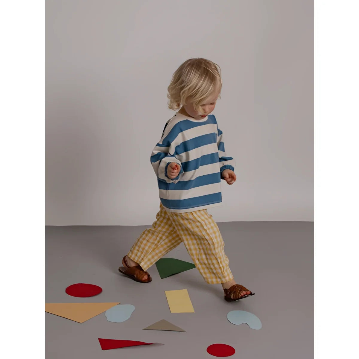 Kind trägt ein sweatshirt deck chair stripes mit blau-weißen streifen und gelb karierten hosen