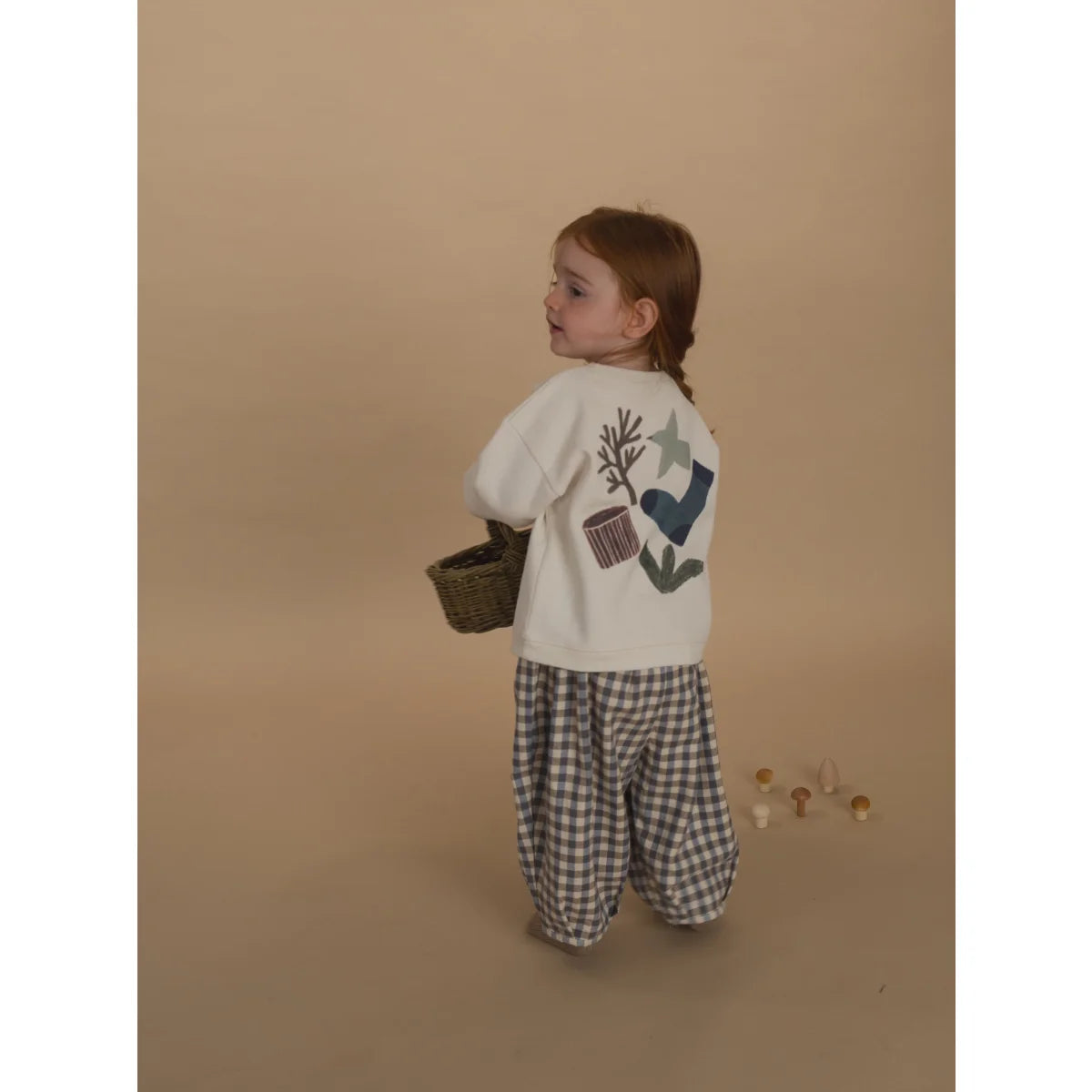 Junge Mädchen in weißem T-Shirt mit Natur-Patches und blauer Karo-Hose mit Korb