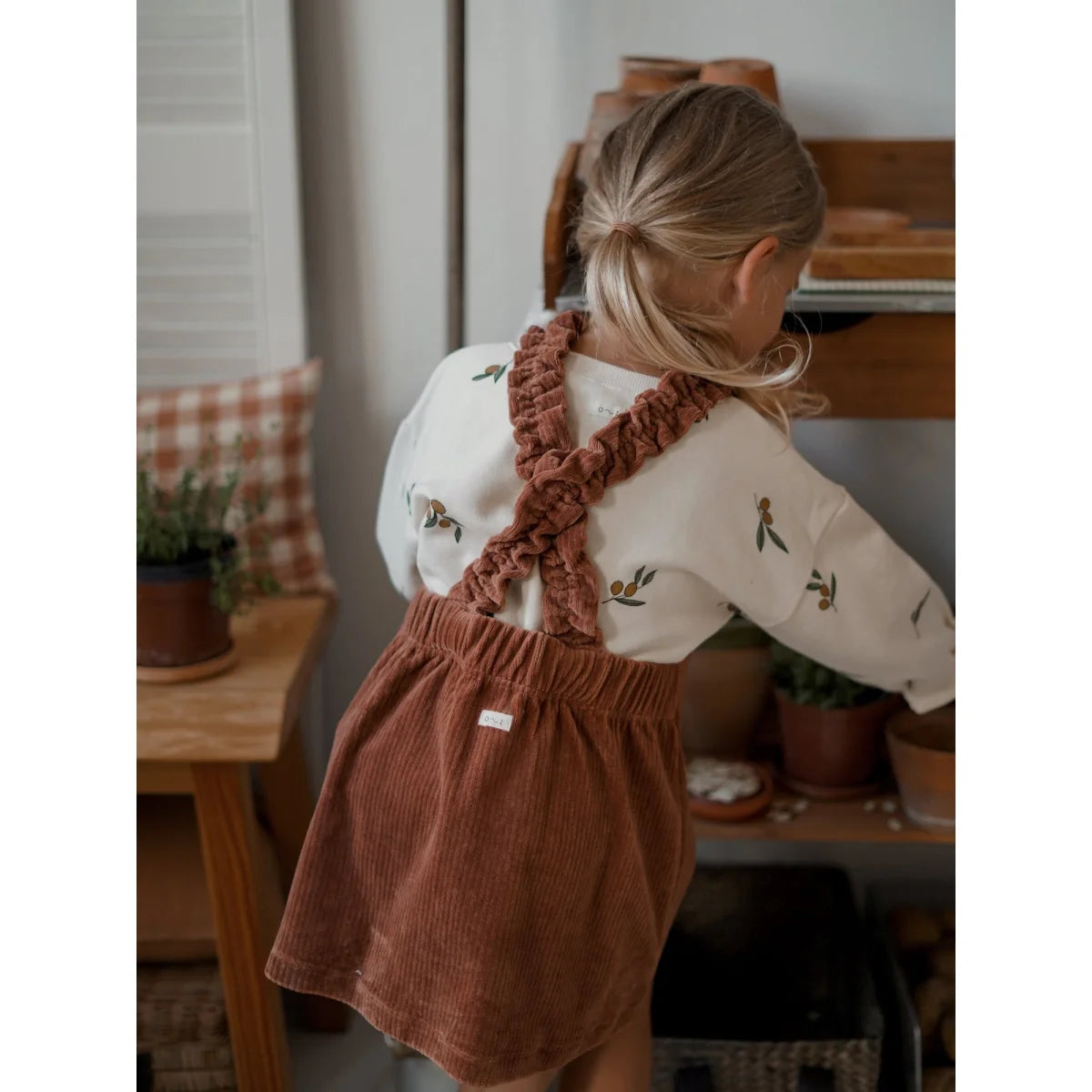 Junger Schüler in weißem Oberteil und rostfarbener Corduroy-Jumperkleid
