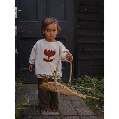 Kind trägt ein weißes T-Shirt mit rotem Blumenmuster und hält einen Korb