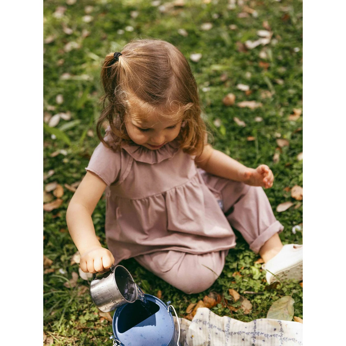 Mädchen in old pink Rüschenkleid gießt Wasser, nachhaltige Babykleidung Schweiz