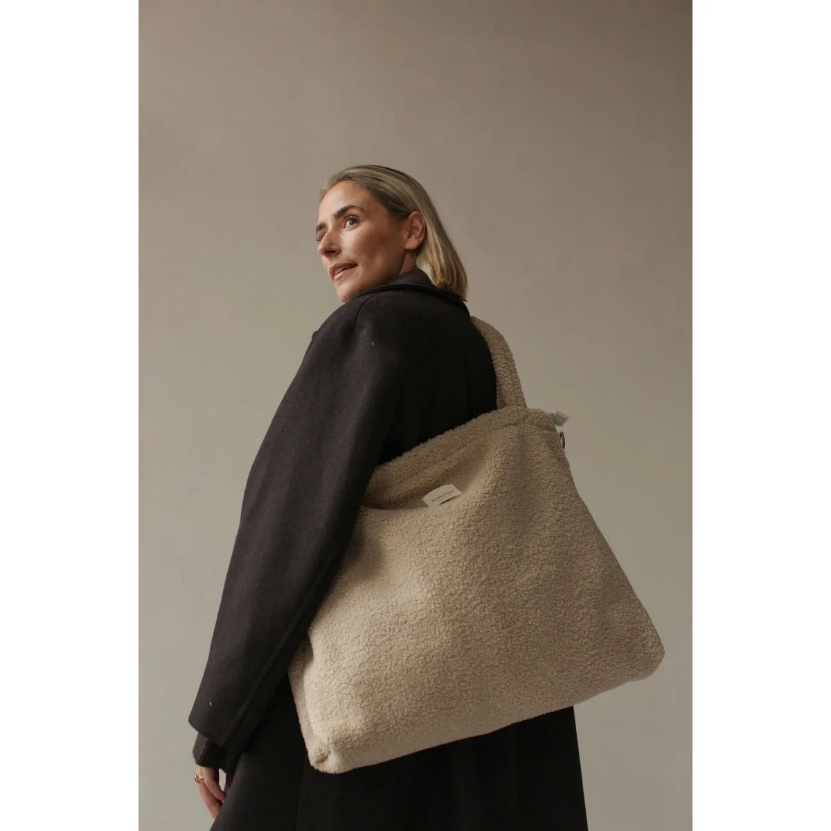Cremefarbenes, strukturiertes Hobo-Bag mit geprägtem Muster über schwarzem Pullover