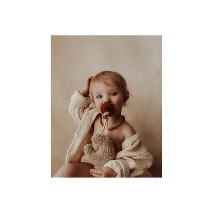 Baby mit Teddy Mond in beige, hält einen Teddybär und benutzt einen Schnuller