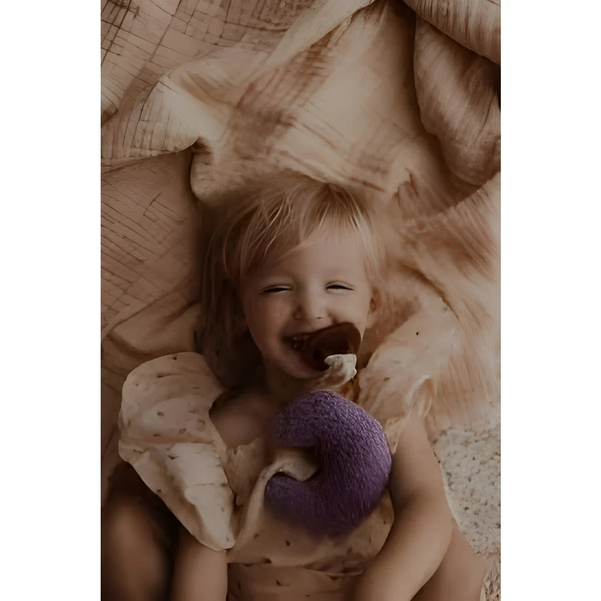 Lachendes Baby mit lila Stofftier auf Stoff, Produkt Teddy Mond | Purple Rain