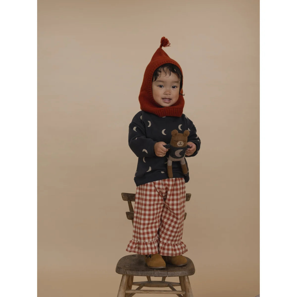 Kind mit rotem gehäkelten Kuschelhut, Mond-Pulli und Karo-Hose vom Teddy Midnight