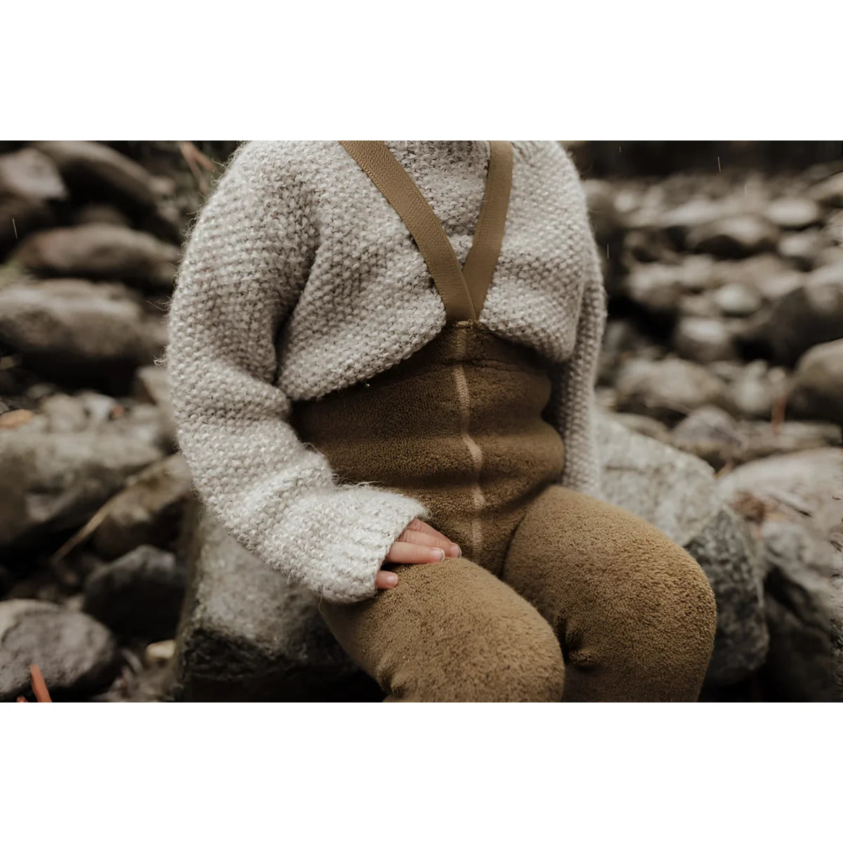 Strick- oder Häkelpuppe in cremefarbenem Pullover und brauen Hosen auf Steinen