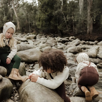Drei Kinder sitzen auf Steinen in der Natur, tragen Teddy Warmy Strumpfhosen