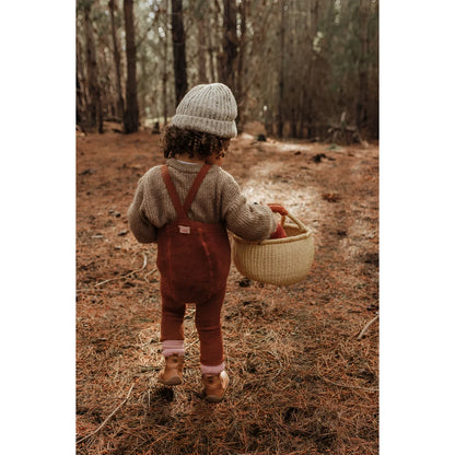 Kind im Overall und Strickmütze trägt einen Korb im Wald für Teddy Warmy Strumpfhose