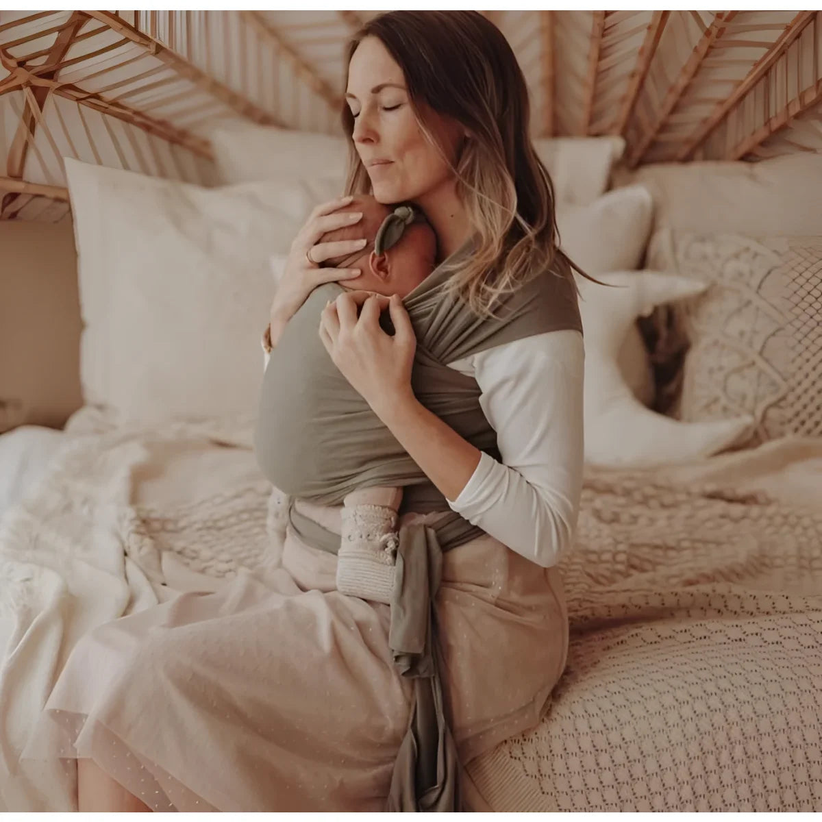 Frau hält Baby in Tragetuch Dusty Olive auf einem Bett