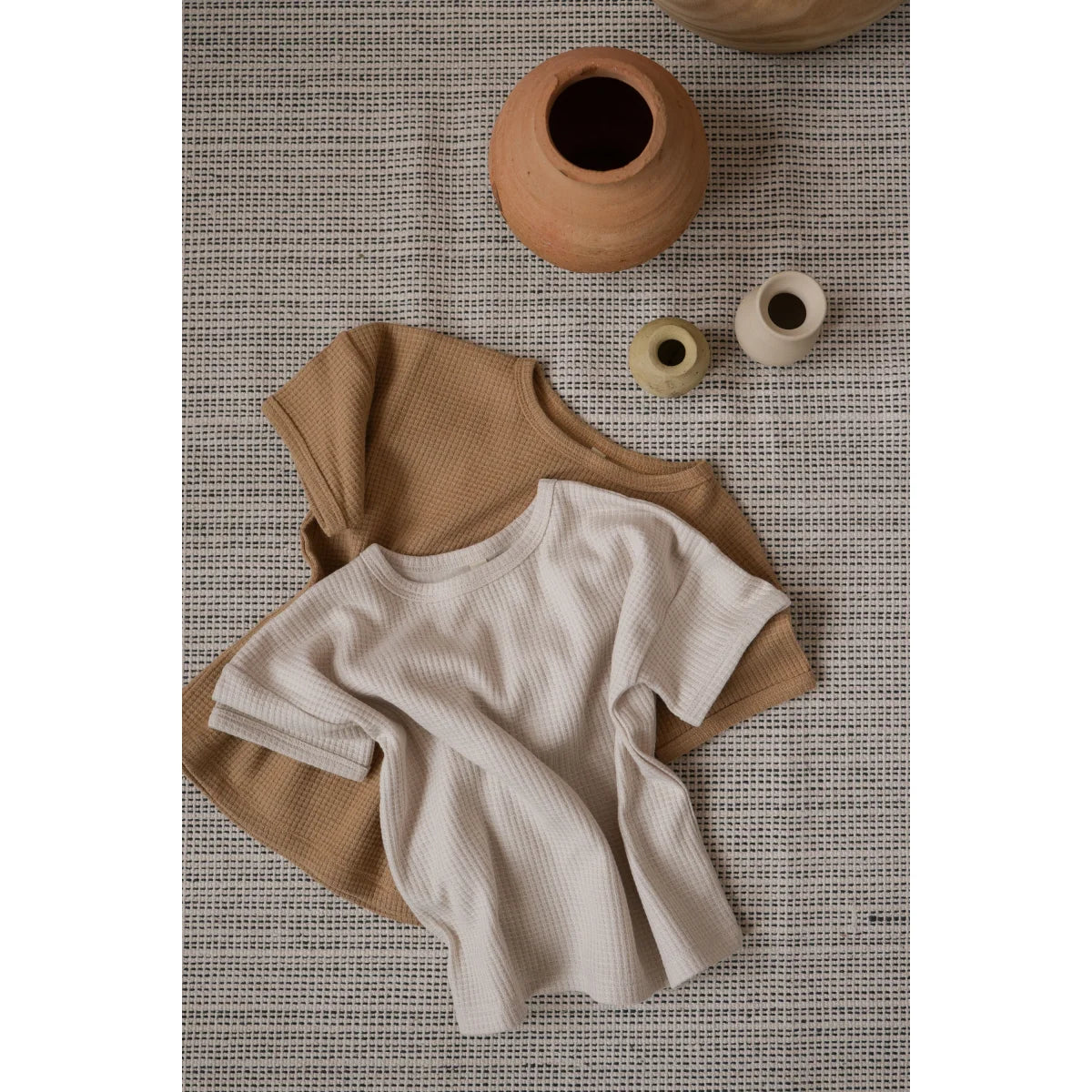 Zwei schlichte T-Shirts in Beige und Creme auf einer strukturierten Oberfläche