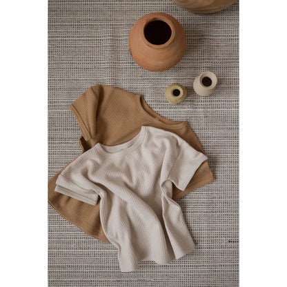 Zwei schlichte T-Shirts in Beige und Creme auf einer strukturierten Oberfläche