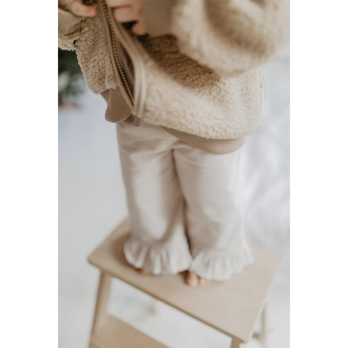 Kindermantel in neutral Tönen mit Rüschen an den Hosen, perfekt für den Winter
