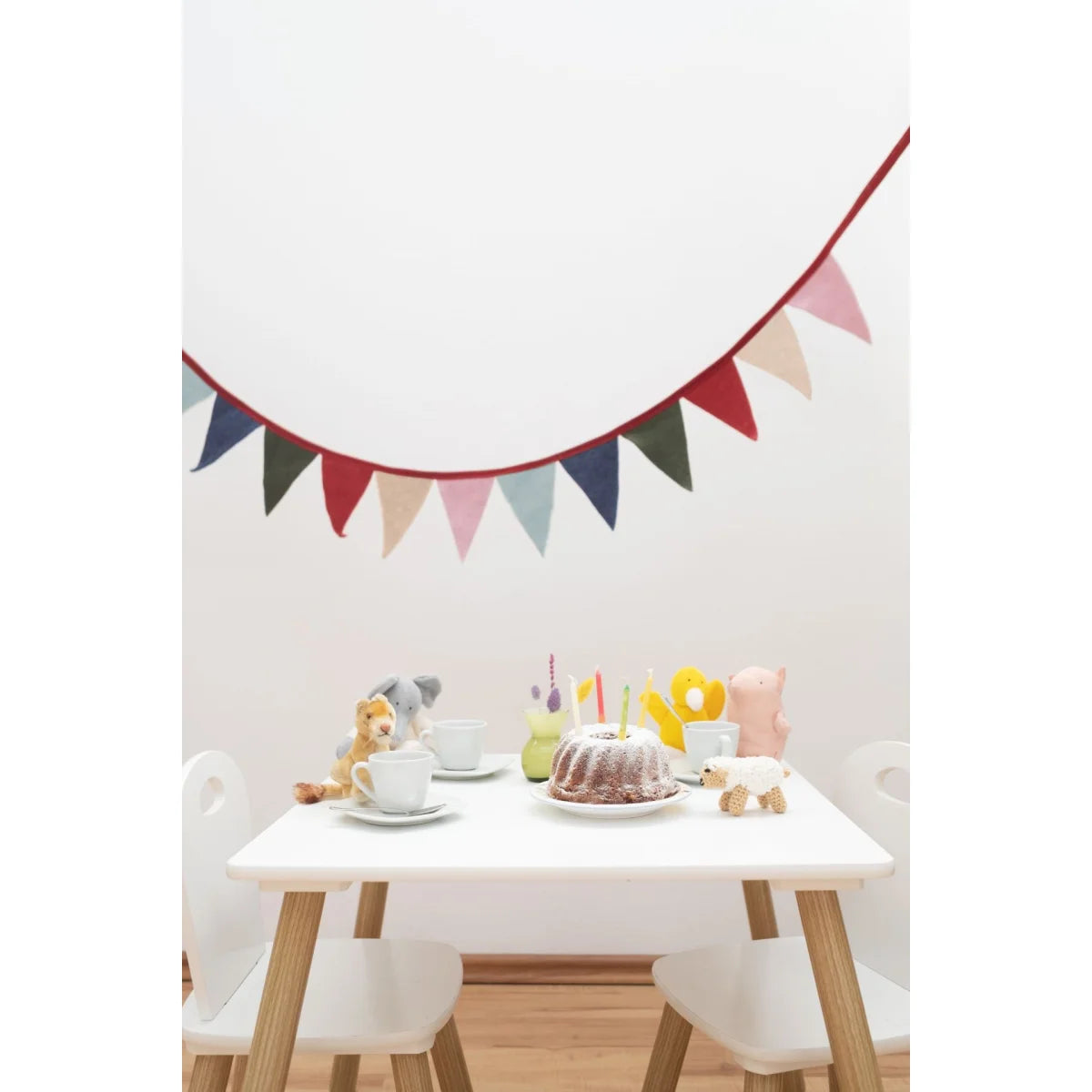 Bunte Wimpelkette mit rotem Rand aus Stoff, hängt über einem Kindertisch an der Wand