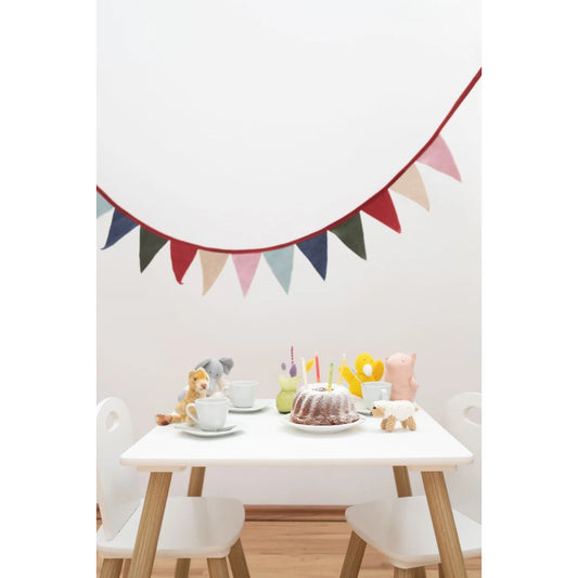 Bunte Wimpelkette mit rotem Rand aus Stoff, hängt über einem Kindertisch an der Wand