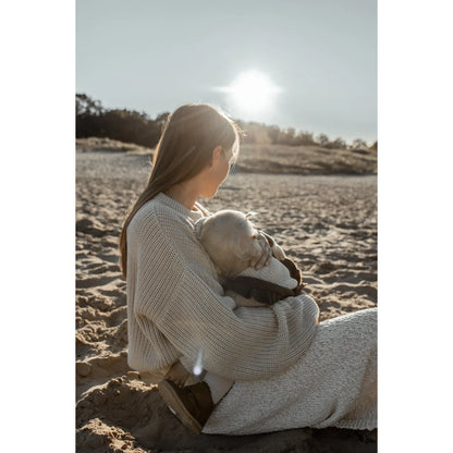 Frau mit Baby am Strand bei Sonnenuntergang in einem grob gestrickten Pullover