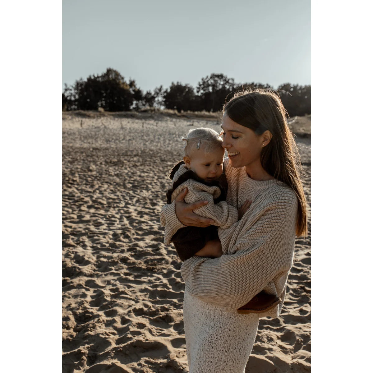Frau hält ein Baby am Strand in einem Frauen Chunky Knit Sweater Oat