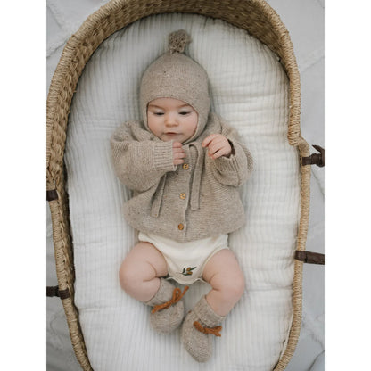 Süßer Säugling in beige gestricktem Wollcardigan, Mütze mit Bommel und Booties