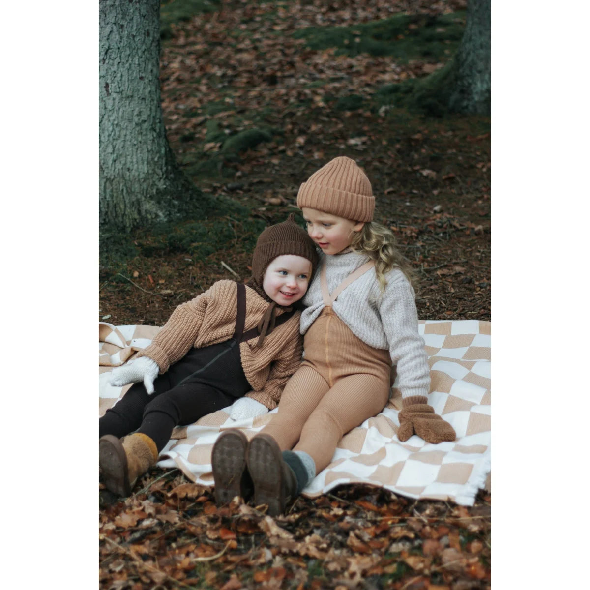 Zwei Kinder auf einer karierten Decke im Herbstlaub mit Wooly Strumpfhosen