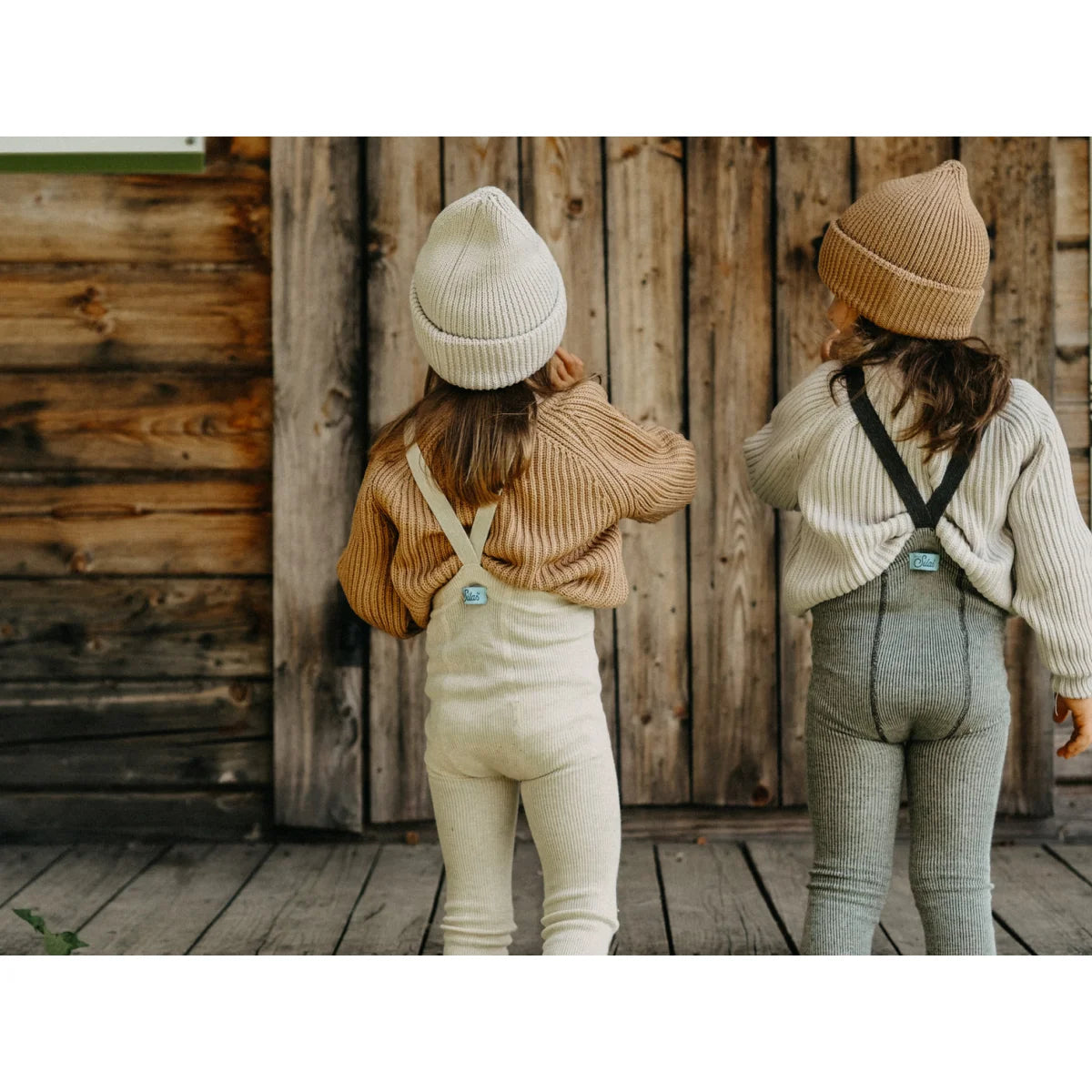 Zwei Kinder in passenden Strickoutfits und Mützen mit Blick von hinten