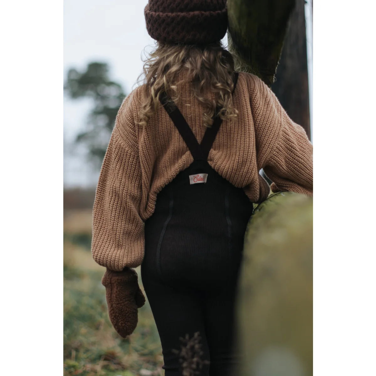 Person mit dickem Strickpullover und dunklem Latzrock in Espressobraun