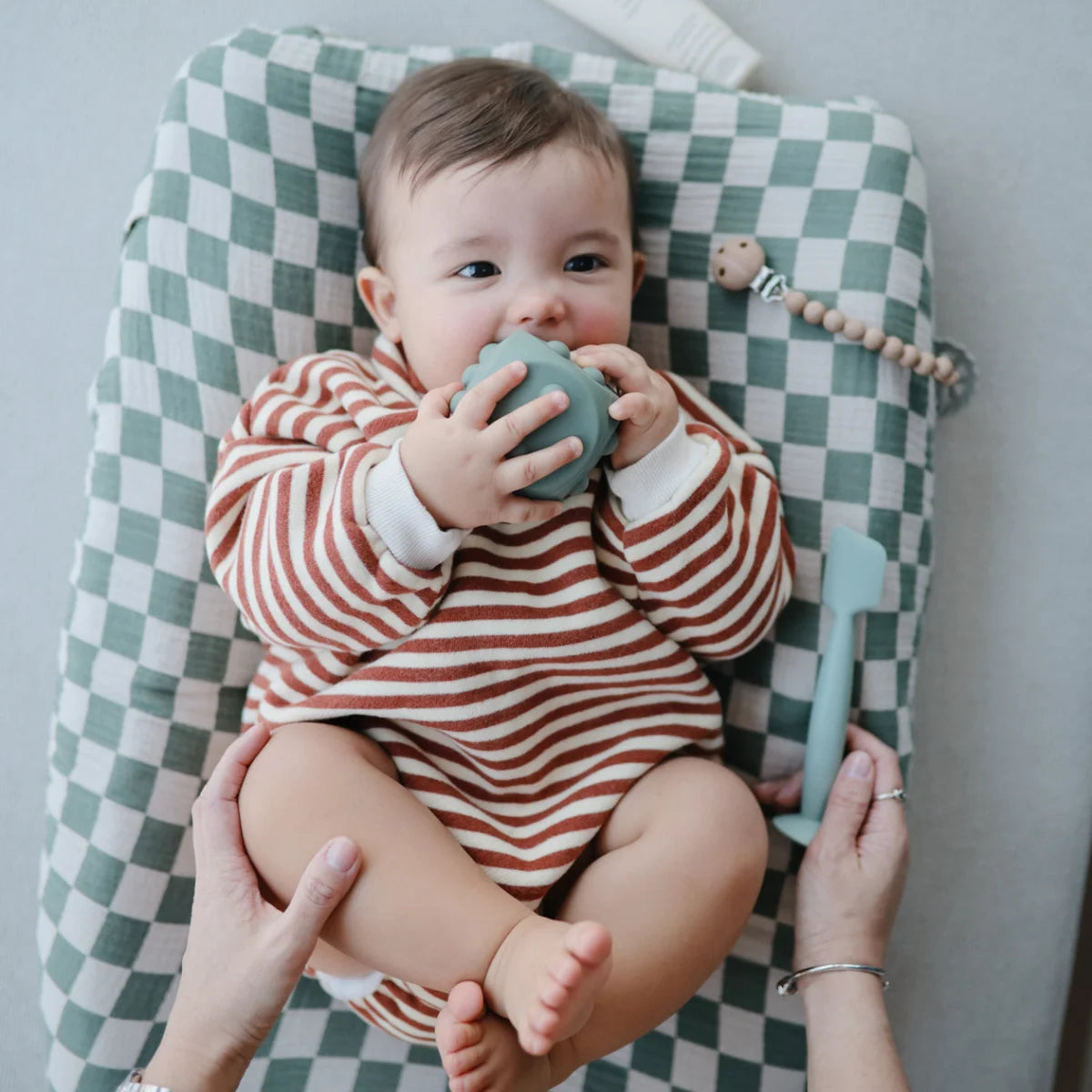 Kleines Baby hält grünes Würfel Plop-it Spielzeug aus Cambridge Blue Shifting Sand